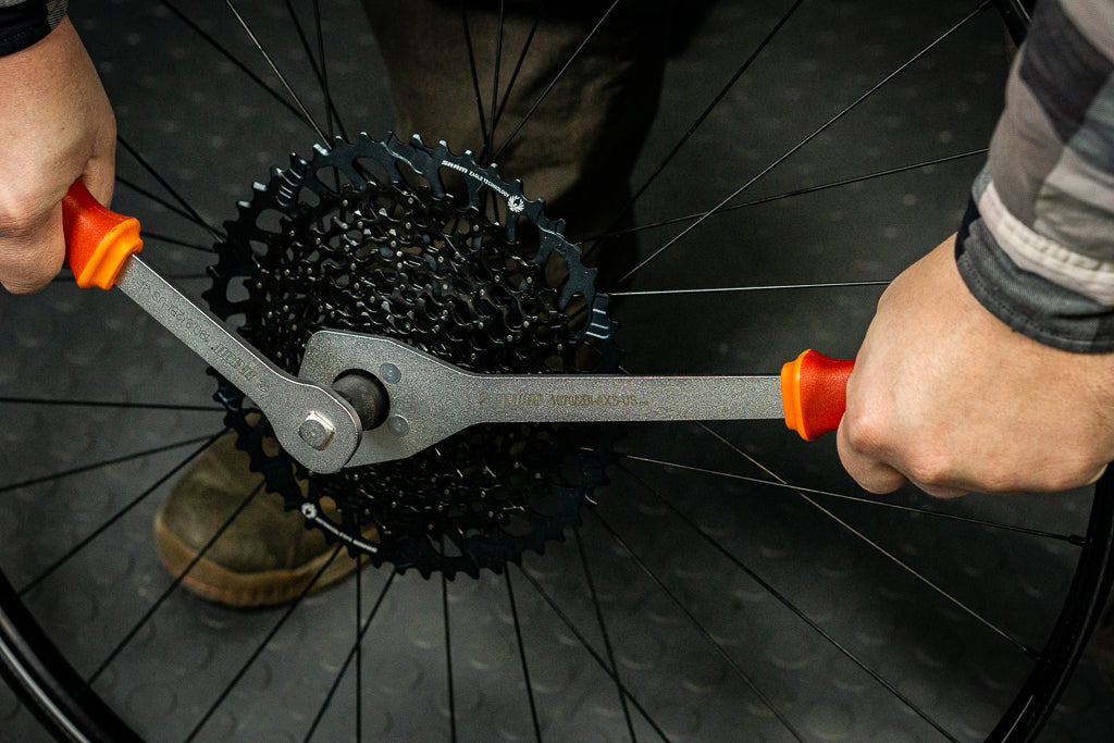 Mechanic loosening a SRAM AXS cassette lockring with the Unior two-handled AXS cassette wrench on a workstand wheel