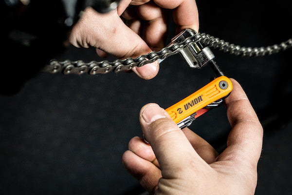 Hands using a Unior multitool to break a bicycle chain in a workshop, folding chain breaker extended from the body