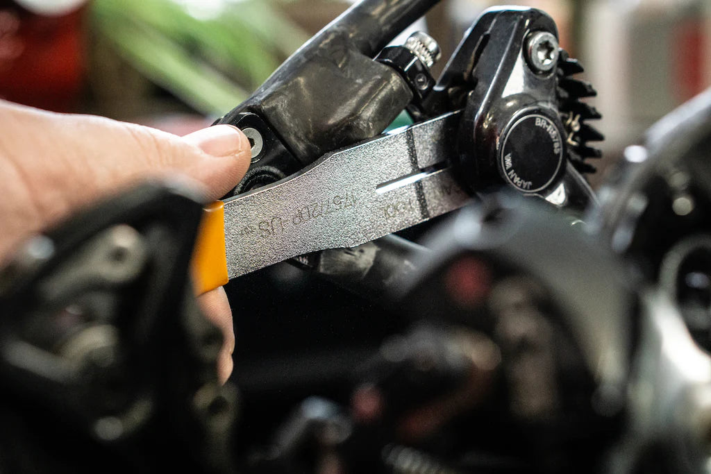 Hand sliding a feeler gauge between brake pads inside a hydraulic disc brake caliper to measure pad wear