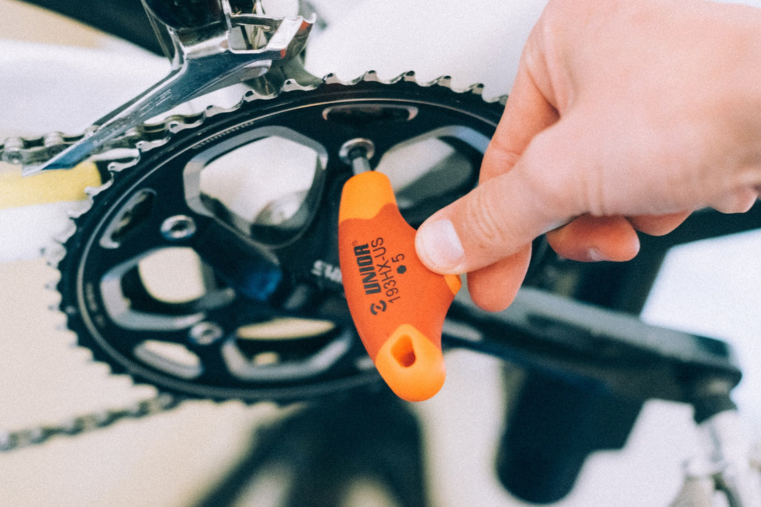Hand holding a Unior 193HX-US 5 mm hex T-handle next to a road bike crankset to check for a creaky bottom bracket