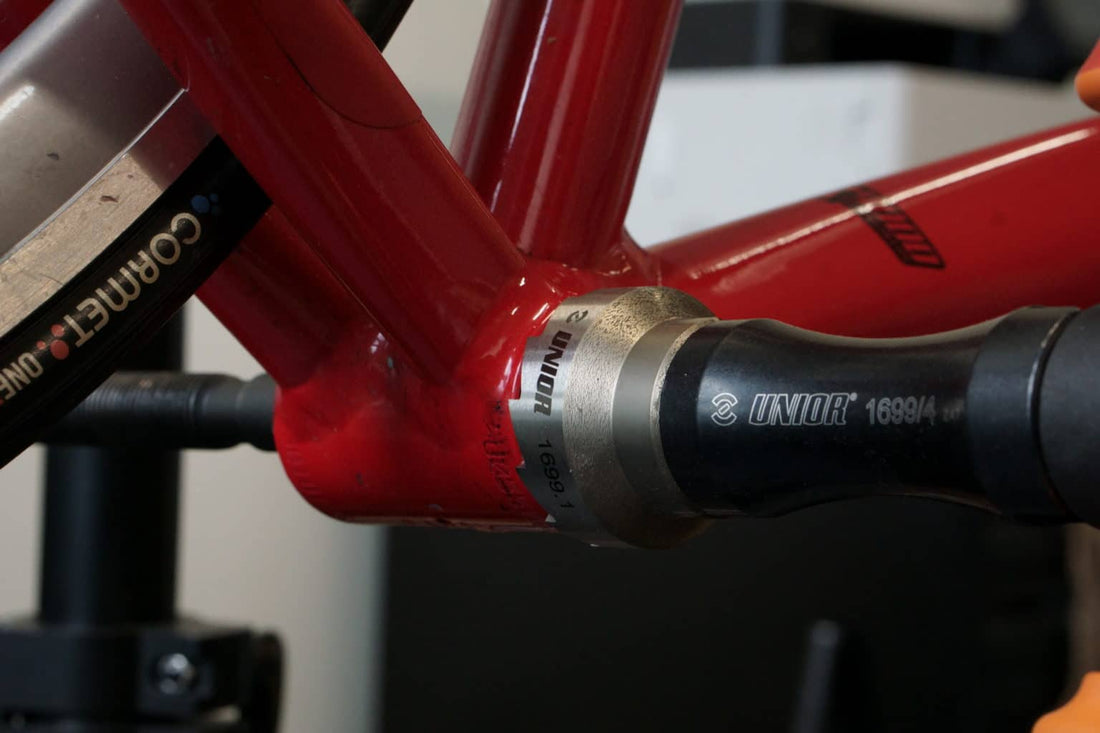 Unior 1699/4 bottom bracket tap engaged in the BSA shell of a red road bicycle frame to chase the threads
