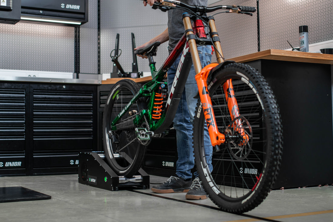 Mechanic bedding in disc brake pads on a Sinter Smart Bedding Machine, downhill mountain bike rear wheel spinning on the bench rollers in a Unior workshop
