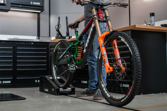 Mechanic bedding in disc brake pads on a Sinter Smart Bedding Machine, downhill mountain bike rear wheel spinning on the bench rollers in a Unior workshop