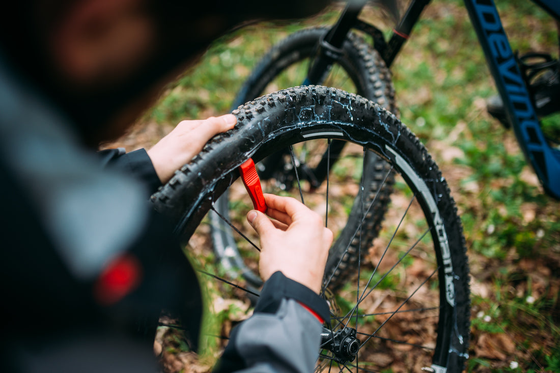 Mechanic seating a tubeless mountain bike tire onto the rim using a red Unior tire lever, outdoor trailhead repair