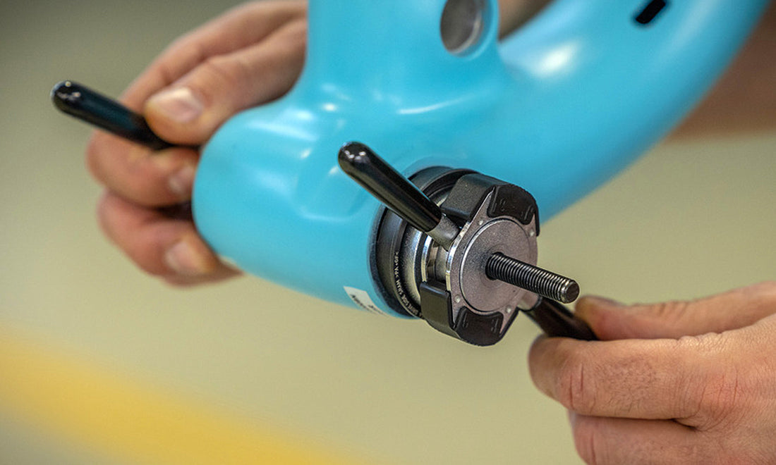 Hands turning a Unior bearing press to seat a press-fit bottom bracket cup in a light blue frame