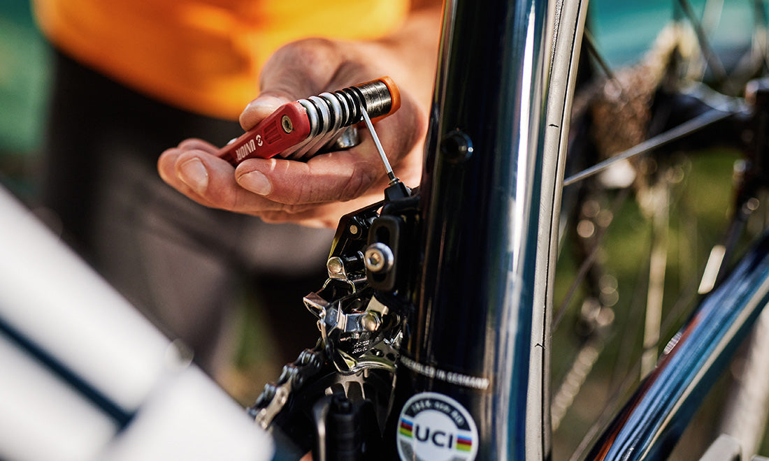 Hand adjusting a front derailleur on a road bike with a red-handled Unior folding tool