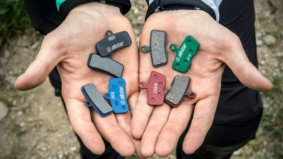 Eight Sinter organic disc brake pads in different fitments and colors held in two open hands