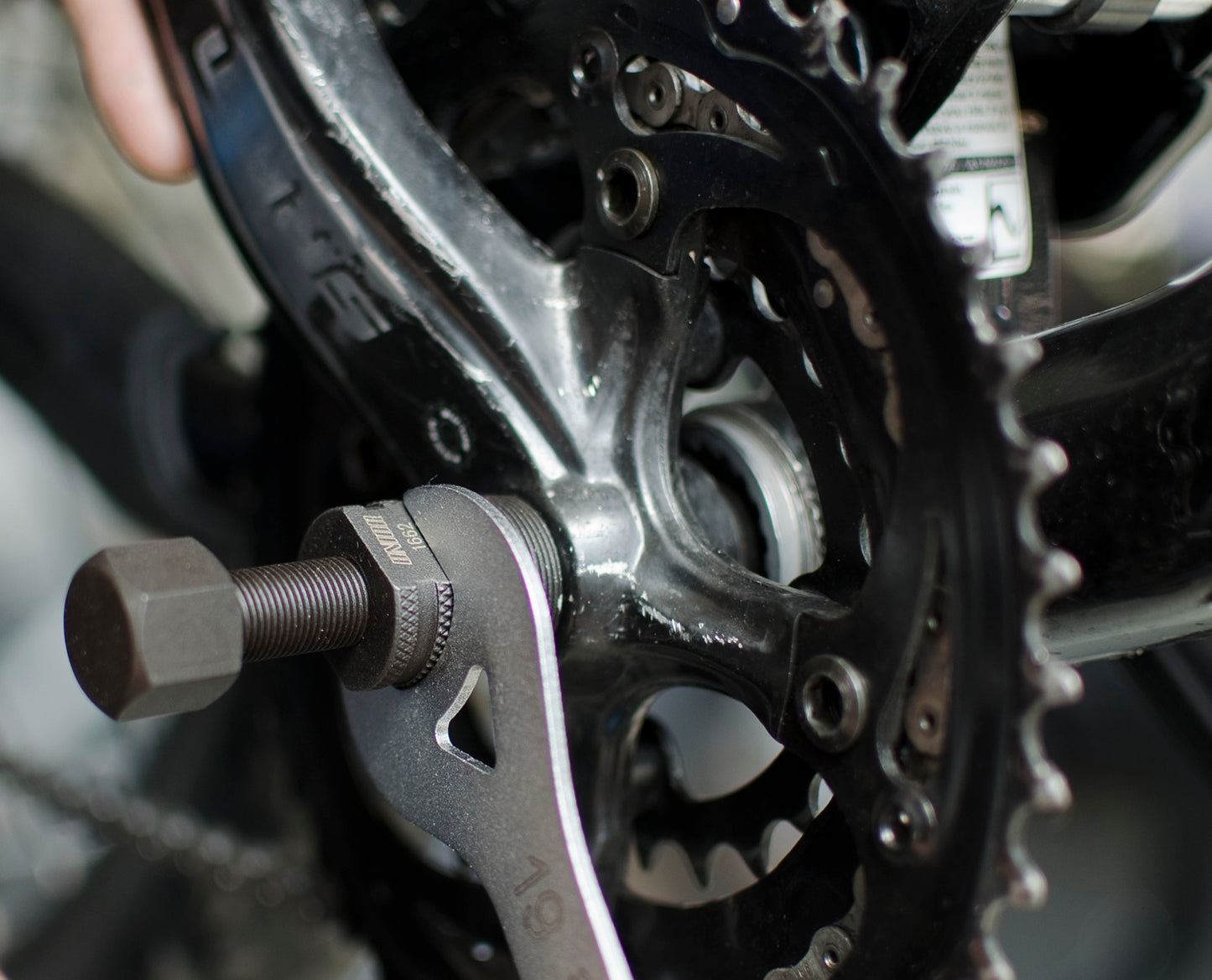 Unior 1662/4 tapered crank puller threaded into a crank arm, held with a 19 mm wrench, centre rod extended