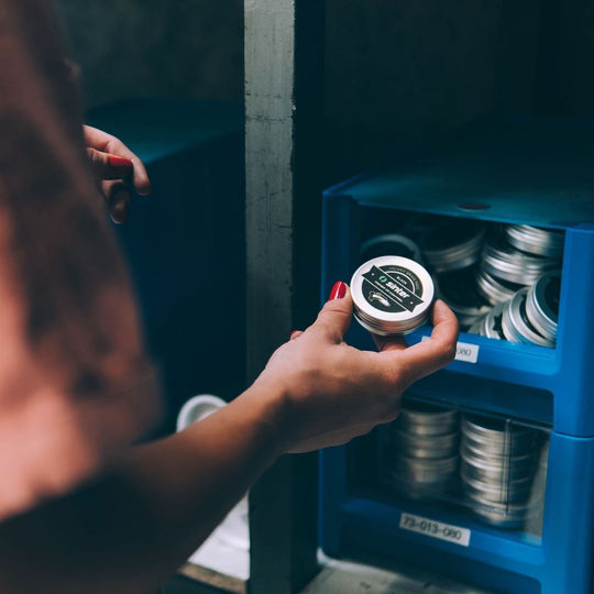 Hand holding a Sinter Black organic brake pad tin in front of a blue parts bin stocked with more pad tins
