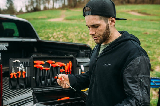 Mechanic checking a tool at an open Unior tool case in a pickup truck bed, T-handle hex keys and pliers visible