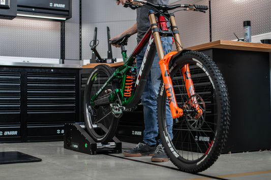 Mechanic bedding in disc brake pads on a Sinter Smart Bedding Machine, downhill mountain bike rear wheel spinning on the bench rollers in a Unior workshop
