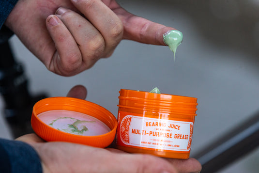 Juice Lubes Bearing Juice multi-purpose grease jar open in a mechanic's hand, fingertip scooping green grease