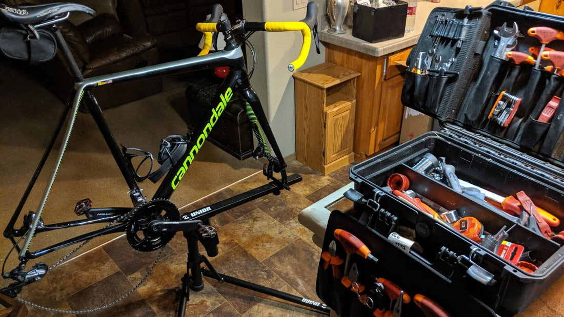 Cannondale road bike on a Unior repair stand beside an open Unior tool case loaded with orange-handled tools