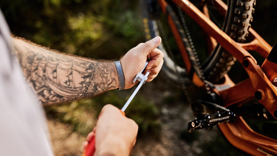 A mechanic using a Unior chain tool on an orange mountain bike's chain outdoors
