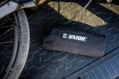 Rolled-up Unior BMX Kit Roll Set 1600BMX-ROLL canvas bag on a vehicle cargo floor next to a bicycle wheel