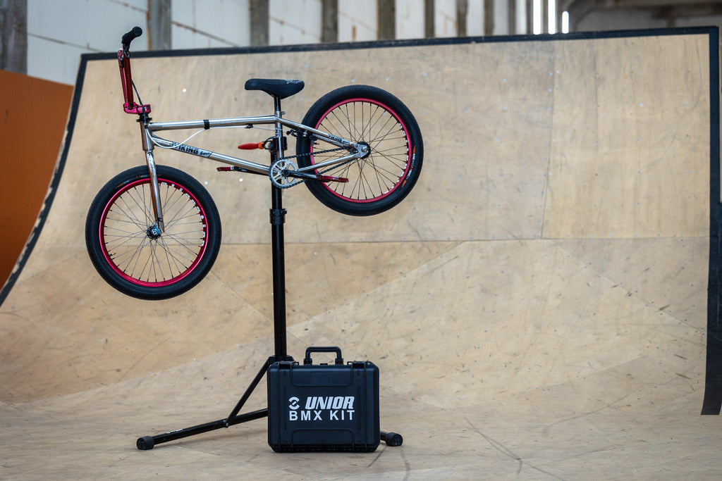 BMX bike mounted on a repair stand in front of a ramp with the closed Unior BMX Tool Kit 1600BMX case at its base