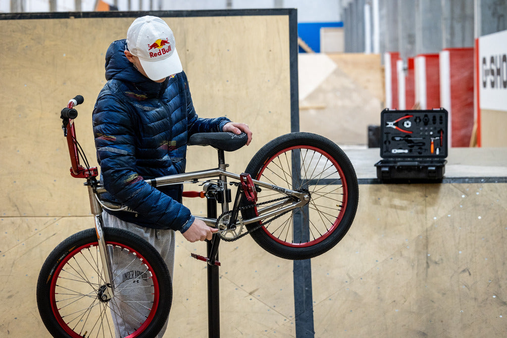 Rider adjusting a BMX bike on a repair stand with the open Unior BMX Tool Kit 1600BMX case on the ramp behind