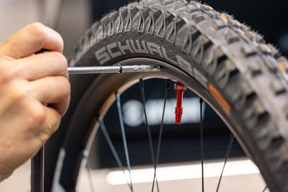 Hanger Genie 2.0 gauge arm aligned to a Schwalbe mountain bike tyre rim, red valve core visible on the wheel