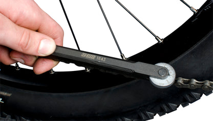 Unior 1643/4 chain wear indicator in use — pins inserted into the chain at the rear wheel while the swing-arm dial is read