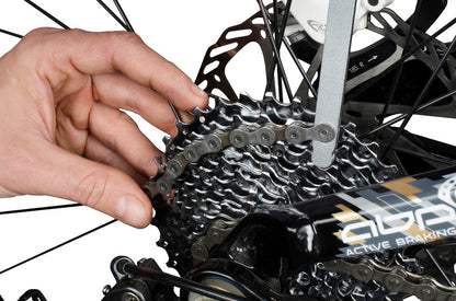 Mechanic using Unior Sprocket Wear Indicator 1658/2P on a rear cassette to measure tooth wear, AVID disc rotor visible