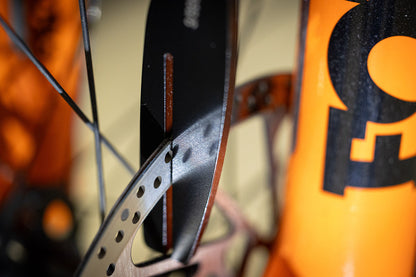 Rotor Truing Fork 2.0 close-up, slotted blade gripping a disc brake rotor on an orange mountain bike for bend correction