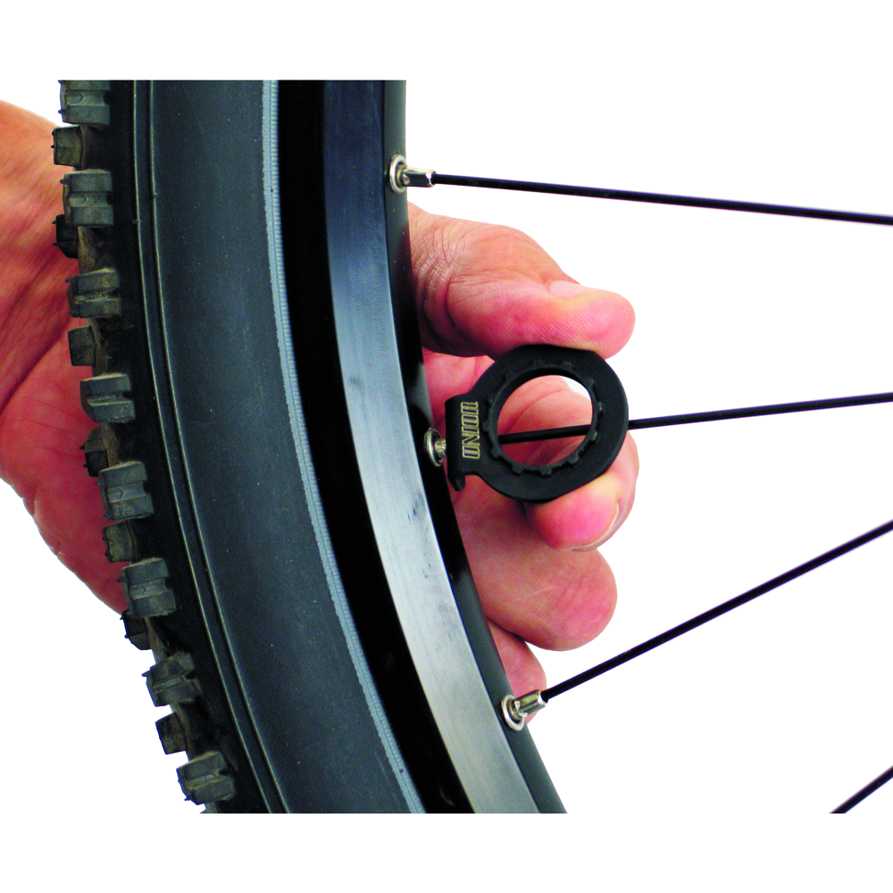 Unior 1669/4 pocket cassette lockring tool held in a hand at a rear wheel, its integrated spoke wrench engaging a spoke nipple; compact trailside cassette and spoke tool