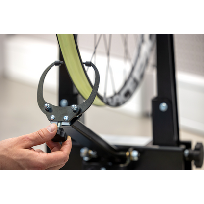 Hand adjusting the Pro Truing Stand 1689 caliper arm on a green Race wheel, indicator finger near the rim