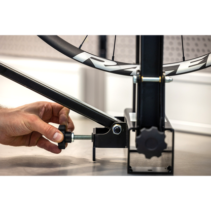 Hand tightening a wing-screw on the Pro Truing Stand 1689 frame, Race-branded carbon wheel mounted above