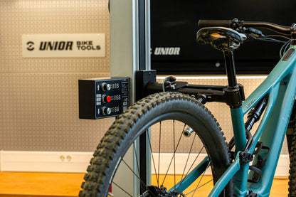 Electric Repair Stand 2.0 holding a Specialized Levo e-mountain bike, control panel showing height-adjust readouts in the workshop