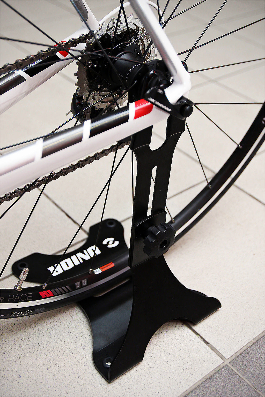 Unior 1693H display stand holding a road bike by the rear-axle slot, rubber-padded tines against the dropout, black finish