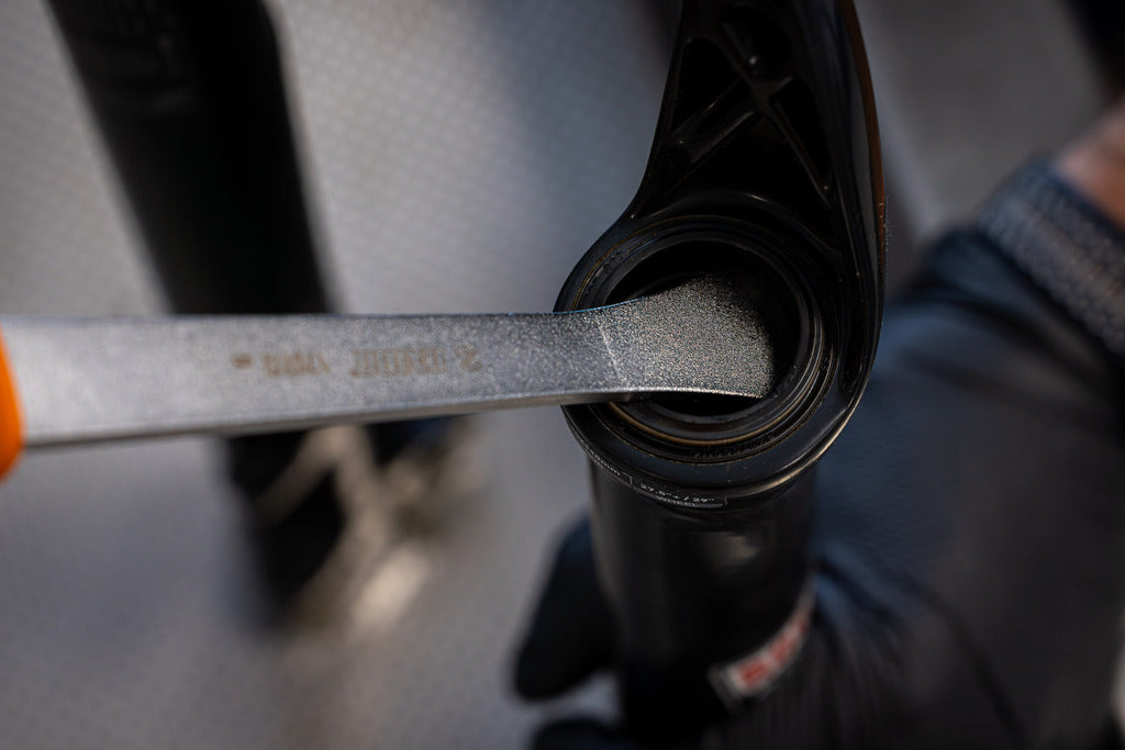 Fork Dust Seal Remover tip wedged under the dust seal of a suspension fork lower, close-up of the prying action
