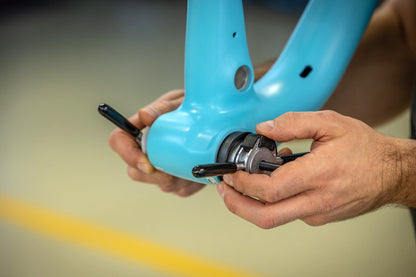 Unior 1721BB bottom bracket press tool engaged in the shell of a blue bicycle frame, T-handles turning the threaded shaft