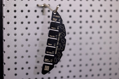 Unior Rotor Wear Indicator hanging on workshop pegboard hook, vertical view of OEM-coded thickness slots and QR tag