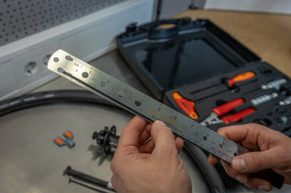 Mechanic holding the Master Wheel Building Kit 1754 spoke-length gauge ruler over a rim and hub on a workbench