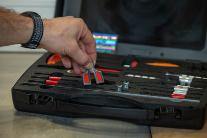 Hand lifting a red Unior spoke tension gauge from the foam tray of the Master Wheel Building Kit 1754 case