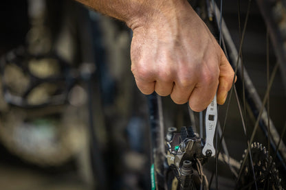 Unior 1760/2 flare nut wrench on the caliper-side fitting of a rear hydraulic disc brake, reaching past rotor and spokes