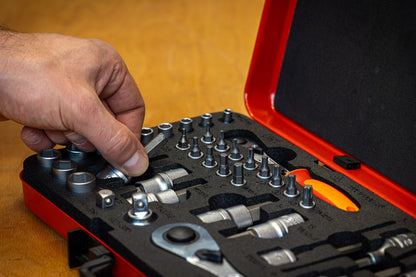 Mechanic lifting a chrome socket from the Unior Master Bits and Sockets Set on a workshop bench, case open beside