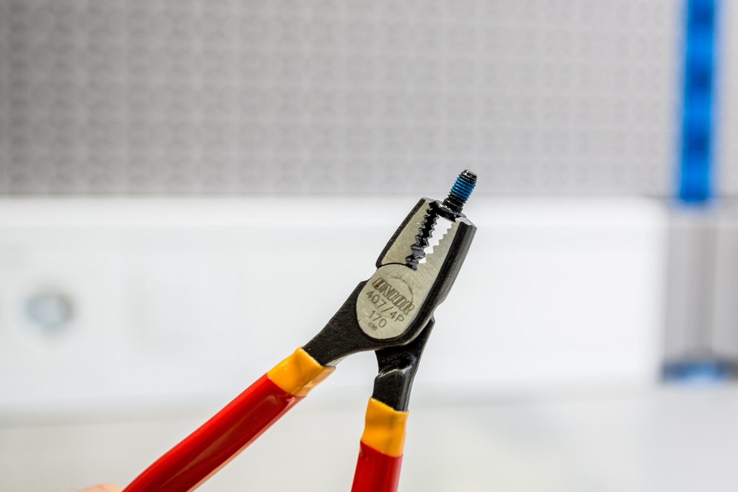 Unior 407/4DP-US screw grabbing pliers gripping a small setscrew by its head, serrated jaws clamped on the outer diameter