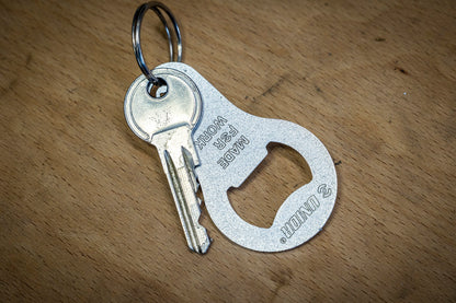 Unior Mini Bottle Opener 45/2A on a keyring with a house key, resting on a wooden workshop bench