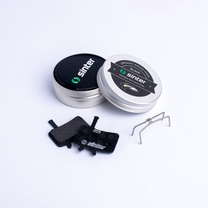 Sinter Model 005 Black organic disc brake pads with retention spring beside aluminium tin packaging for Avid calipers