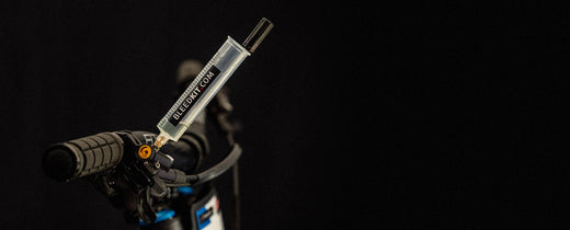 Bleedkit syringe attached to a mountain bike brake lever during a hydraulic bleed, dark workshop background