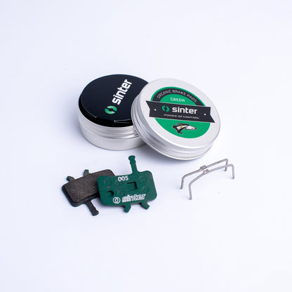 Sinter Model 005 Green organic disc brake pads with retention spring beside aluminium tin packaging for Avid calipers
