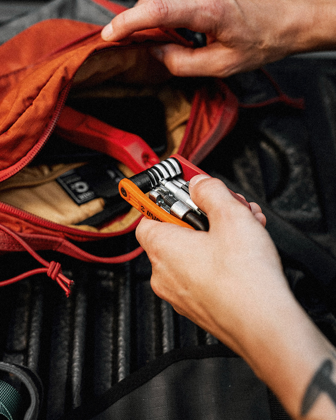 Multitools category thumbnail showing a cyclist unfolding a Unior multitool over an orange pack at a trailhead