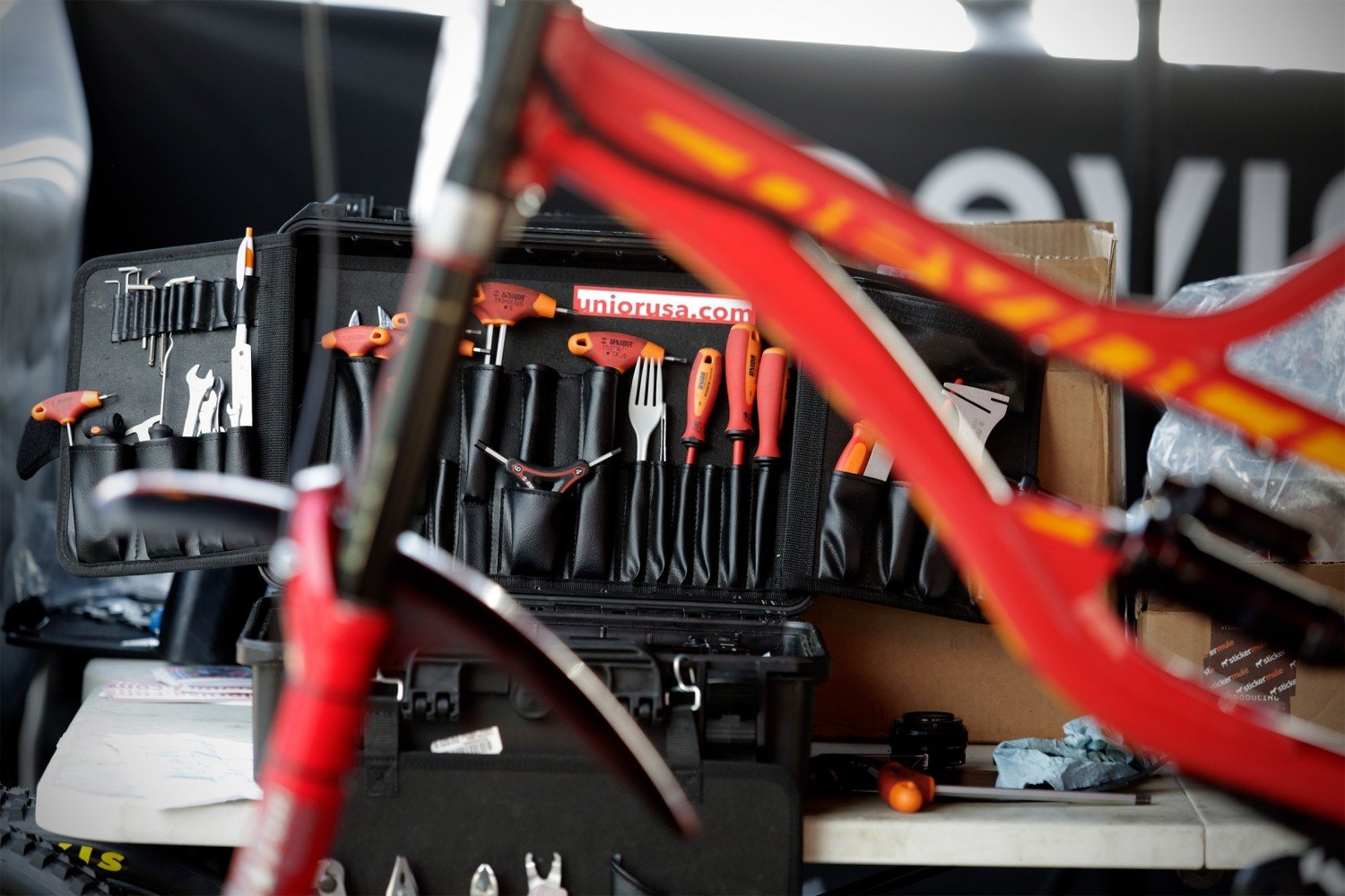 Unior USA race mechanic's tool case open in the pits, red-handled Unior tools laid out behind a bike frame