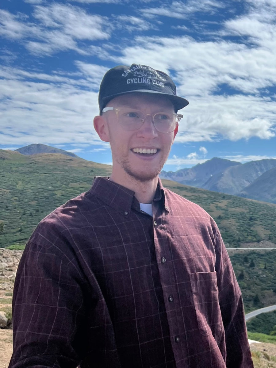 Unior USA team member portrait, young man in a cycling club cap and plaid shirt with mountain landscape behind
