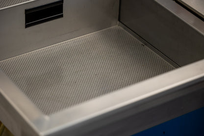 Close-up of empty stainless basin inside the Unior 990SIN suspension sink, perforated drain floor and drain slot visible