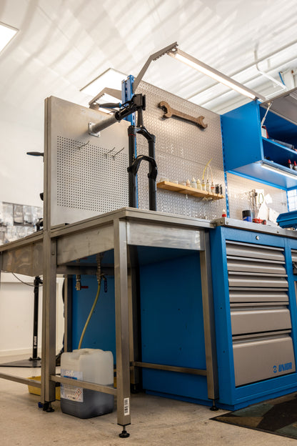 Unior 990SIN suspension sink installed at a workbench with overhead light arm, suspension fork clamped for service