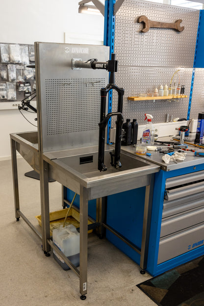 Unior 990SIN suspension sink installed in a workshop, mountain bike fork clamped above the basin beside a blue tool cabinet