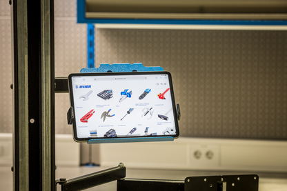 1693EL.6 tablet holder in use on a Unior workstand, tablet displaying the Unior bike tools catalog in a workshop