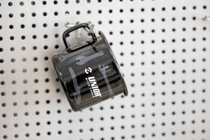 Unior Bike Tools enameled mug hanging by handle on a workshop pegboard, side of mug printed with wrench graphics